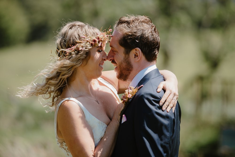 the bride and groom stand face to face in the Perthshire countryside with a loch and hills visible in the background before their Monachyle Mhor wedding in Scotland