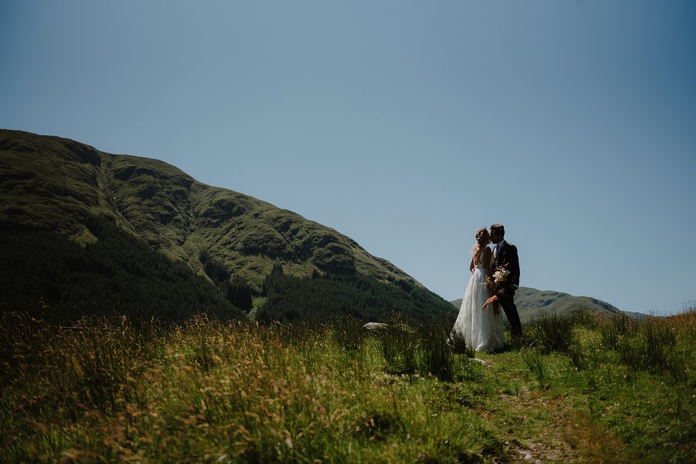 the bride and groom embrace before their Monachyle Mhor wedding ceremony in Perthshire in Scotland hills and blue sky are visible in the background
