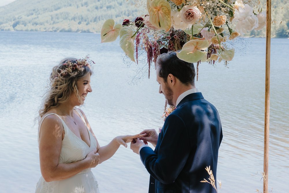 the groom places the wedding ring on the brides finger during their Monachyle Mhor wedding ceremony in Perthshire Scotland