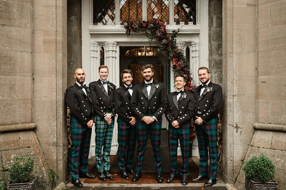 groom and groomsmen standing outside drumtochty castle dressed in kilt and tartan trews