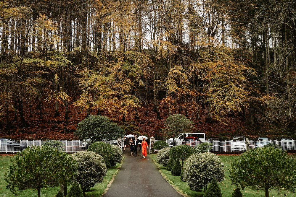 guests arriving for a wedding at drumtochty castle walking through gardens with autumnal forest behind them before a ceremony planned by a Scottish destination wedding planner