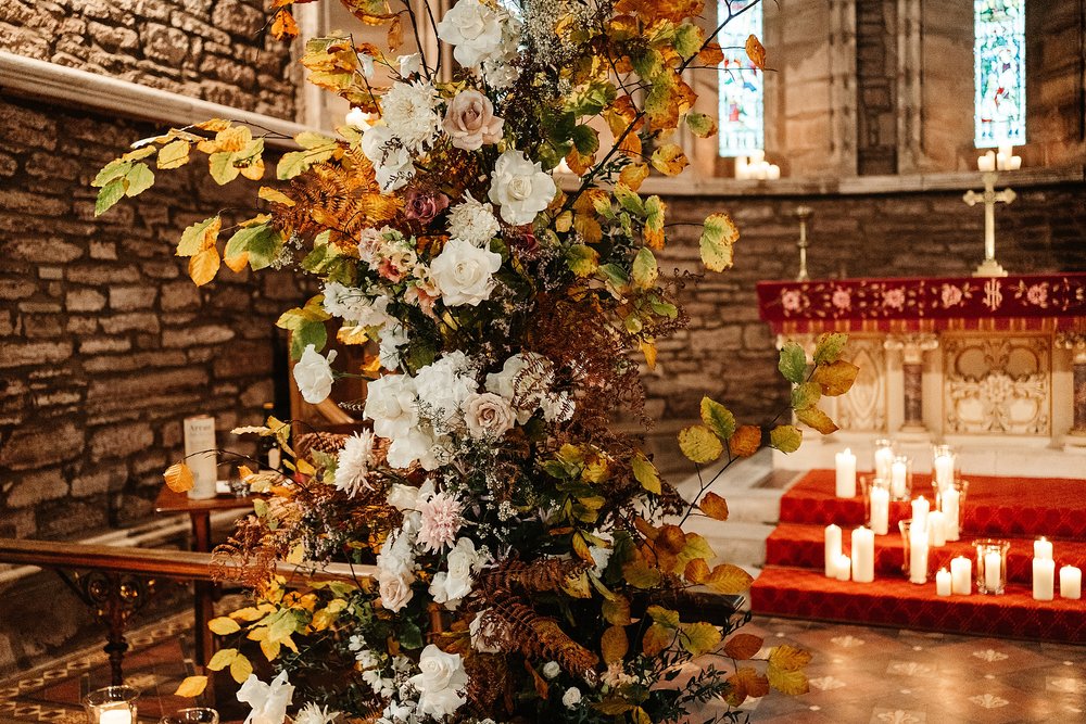 autumnal wedding flower arch with candles inside church near drumtochty castle for wedding by Scottish destination wedding planner