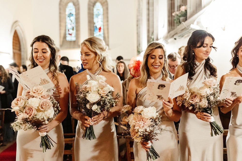 bridesmaids in blush silk dresses and white &amp; blush flower bouquets during wedding in church planned by Scottish destination wedding planner