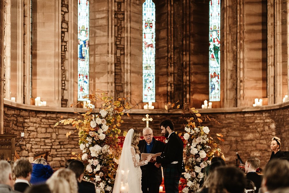 bride and groom saying their vows at the altar in Scottish church with candles and autumn flowers during wedding by a Scottish destination wedding planner