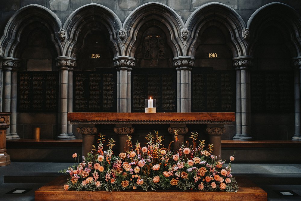 inside glasgow university memorial chapel wedding with a view of the altar dressed with autumnal flowers before the couple's diy wedding venue scotland reception at barrowlands