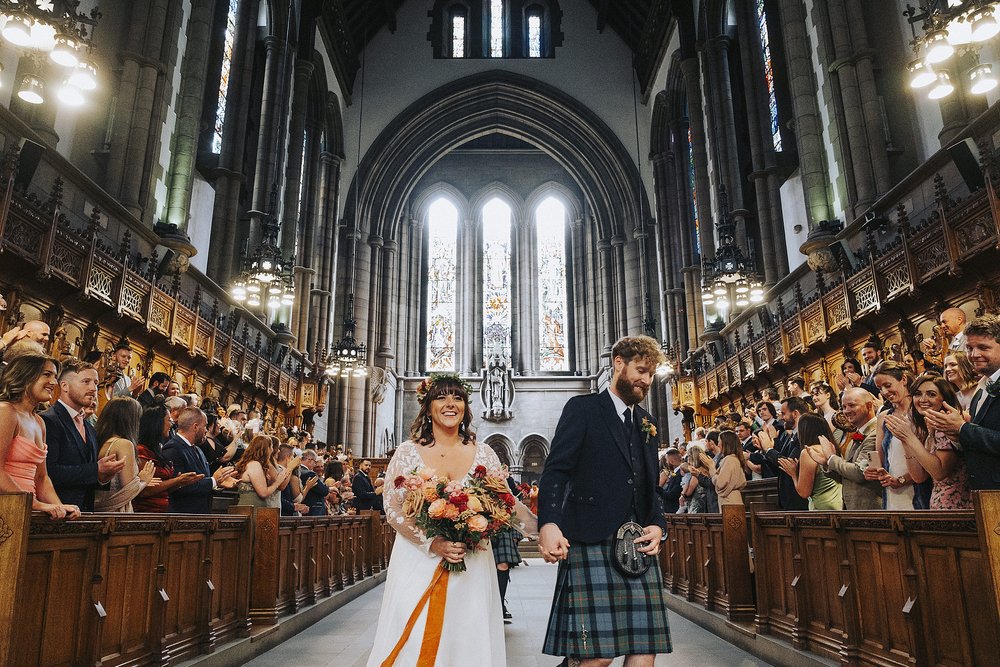 bride and groom walking down the aisle after getting married at glasgow university memorial chapel before the couple's diy wedding venue scotland reception at barrowlands