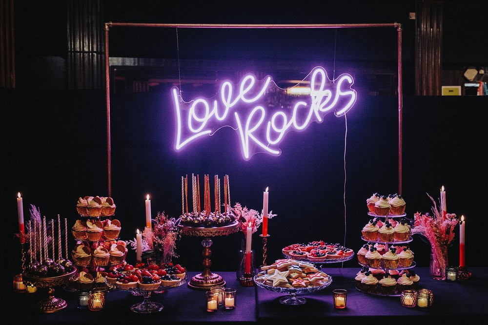 inside barrowlands which is a diy wedding venue scotland showing a luxury dessert table set up below a neon sign saying love rocks