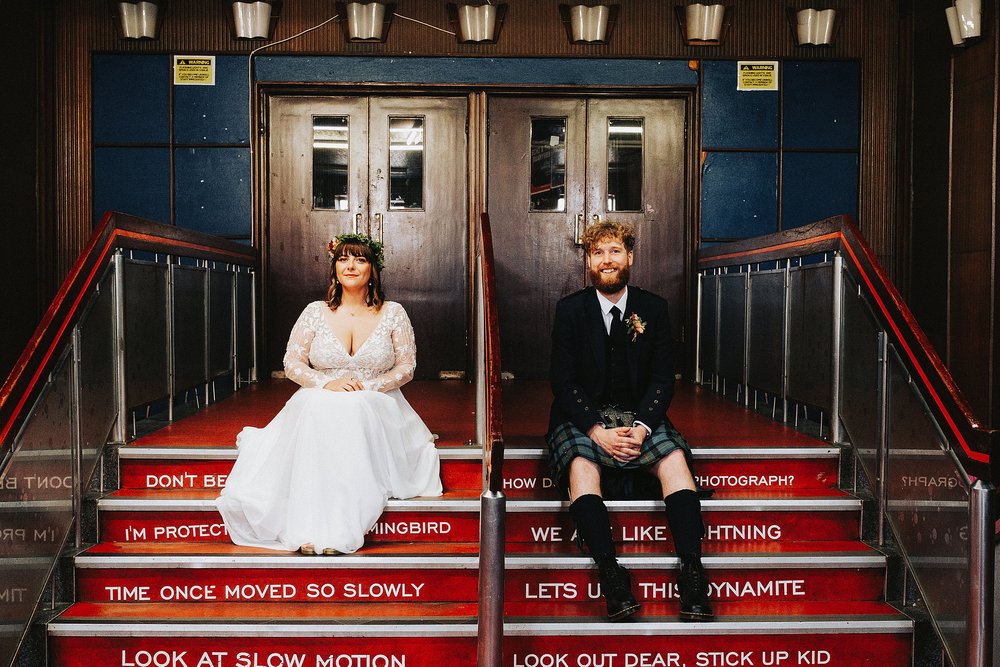 bride and groom sitting on the steps inside barrowlands which is a diy wedding venue scotland