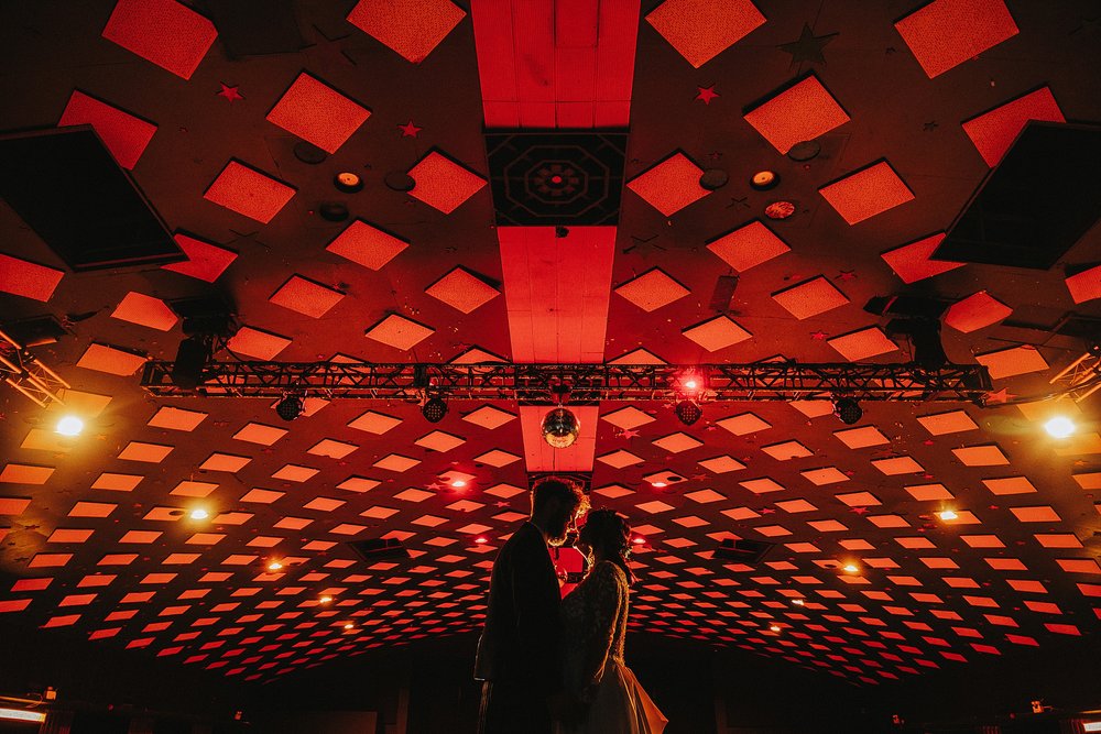 bride and groom in the ballroom underneath red lights inside barrowlands which is a diy wedding venue scotland
