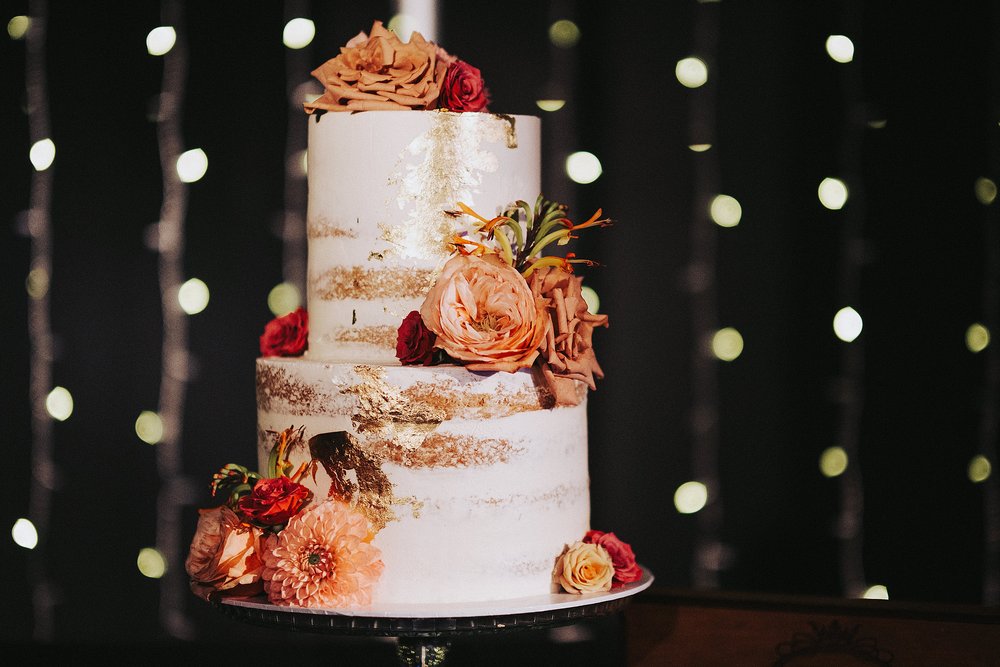  white wedding cake with autumnal flowers sitting in front of twinkling fairy lights at barrowland wedding glasgow 