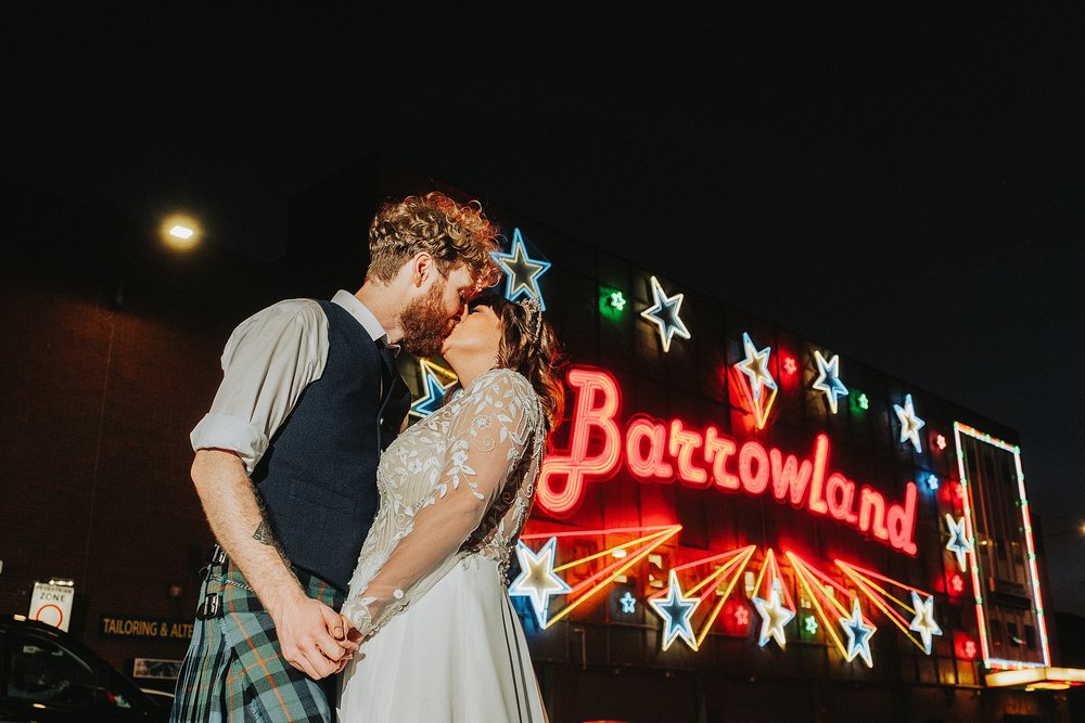 bride and groom outside barrowland glasgow at night with the huge neon sign kissing during their party at the diy wedding venue scotland