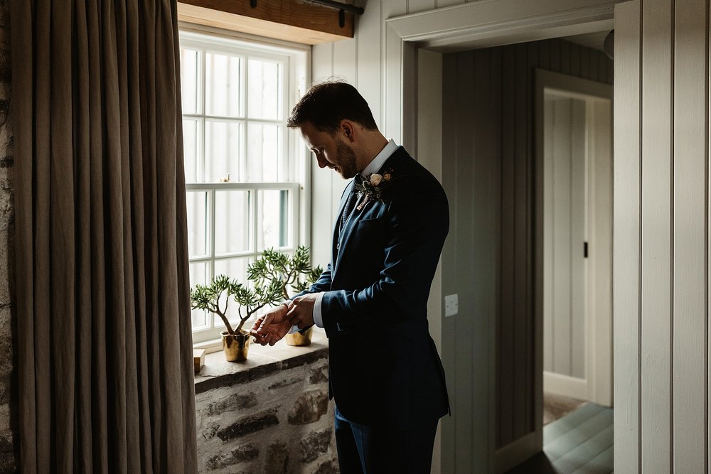 groom standing by a cottage window checking his cufflinks on the morning of his wedding by Scottish highlands destination wedding planner