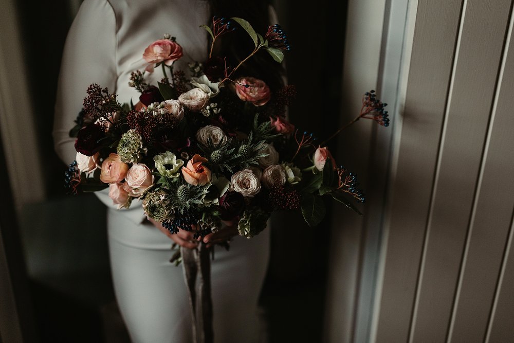 bride holding her bouquet of flowers in peaches whites pink and maroon by wild gorse for an elopement by Scottish highlands destination wedding planner