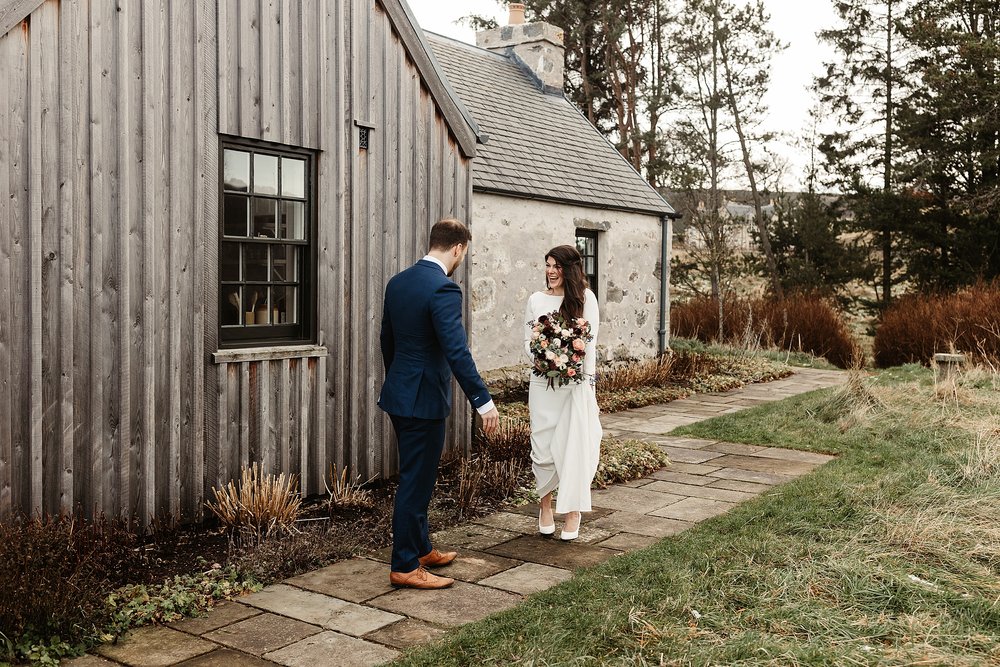 bride in a white gown and groom in a navy suit during their first look outside killiehuntly cottage on the morning of their elopement by Scottish highlands destination wedding planner