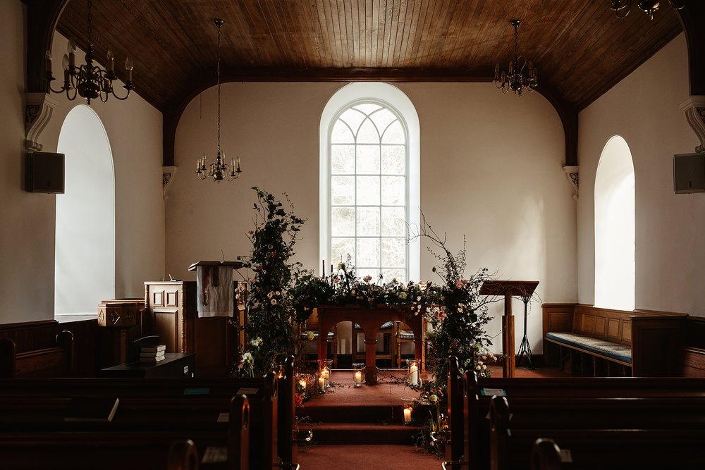 inside of Alvie and insh church decorated with a floral installation of wild flowers and foliage by wild gorse for their elopement by Scottish highlands destination wedding planner