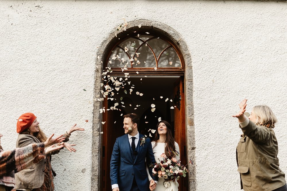 bride and groom walking out of Alvie and insh church under a confetti throw after their Scottish elopement ceremony