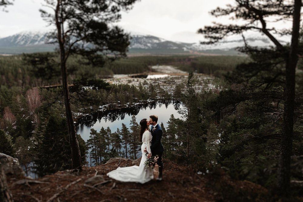 bride and groom standing in a forest with an epic view over a loch in the cairngorms on their wedding day by Scottish highlands destination wedding planner