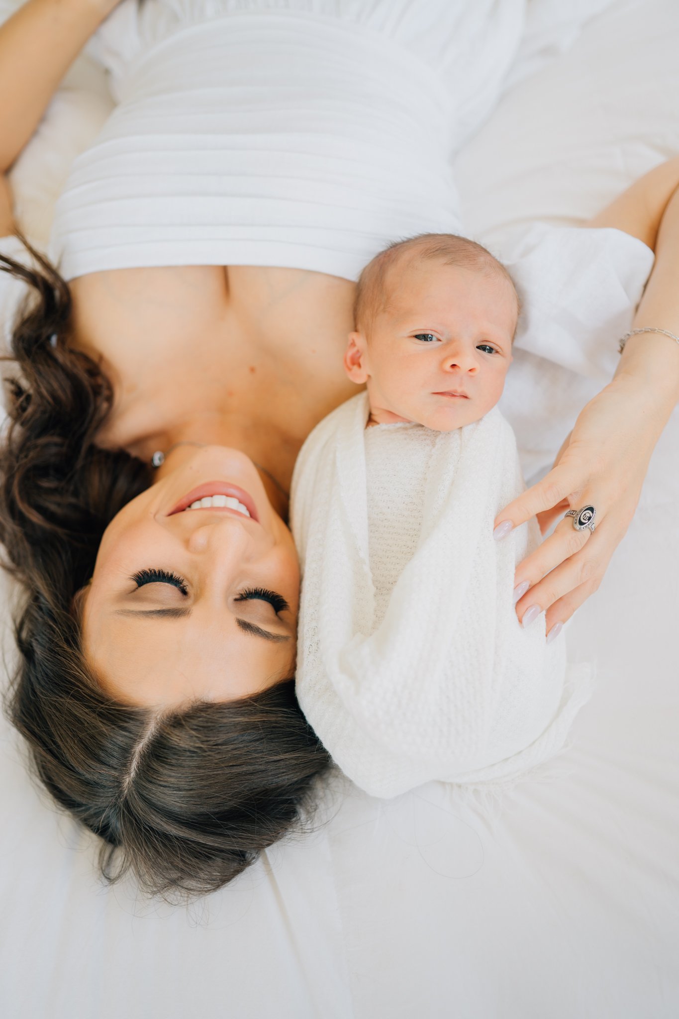 A woman lying on a bed with a newborn baby wrapped in a white blanket, both resting peacefully.