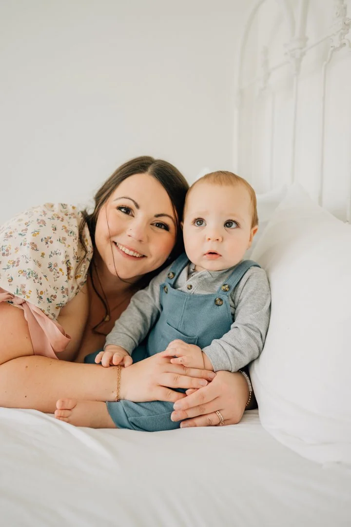  Parents sitting close with their baby in a bright Greenville natural light studio, soft neutral tones and joyful expressions.  Close-up profile of a one-year-old baby looking toward window light in a calm Greenville studio.  Father lifting his baby 