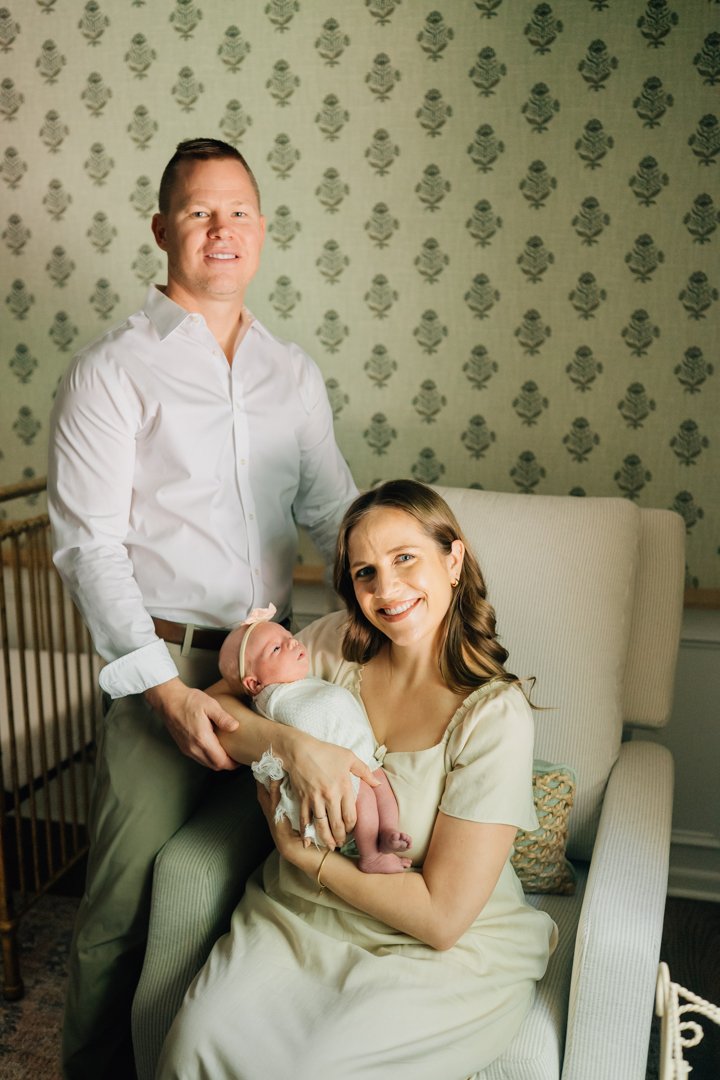    Travelers Rest in home newborn photographers capturing baby Charley with her parents in her nursery    Baby girl newborn photos with parents in a Travelers Rest SC nursery    Mom holding swaddled newborn baby girl beside an antique brass crib in T