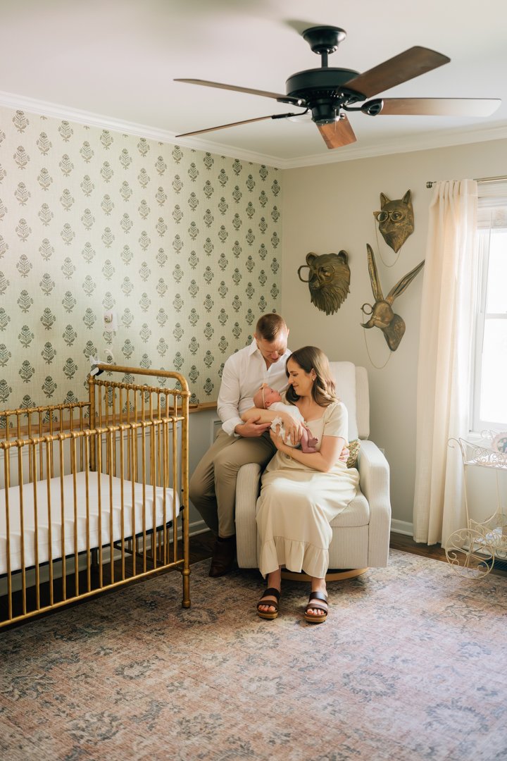    Travelers Rest in home newborn photographers capturing baby Charley with her parents in her nursery    Baby girl newborn photos with parents in a Travelers Rest SC nursery    Mom holding swaddled newborn baby girl beside an antique brass crib in T