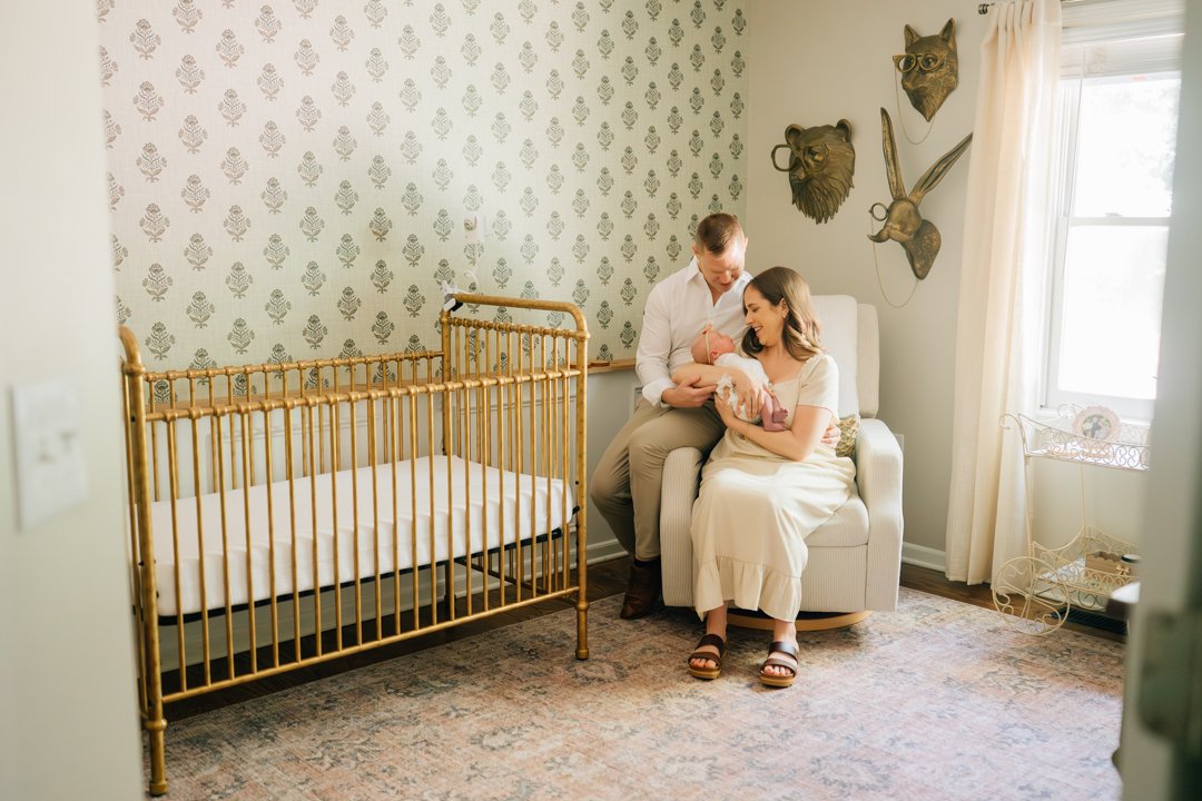    Travelers Rest in home newborn photographers capturing baby Charley with her parents in her nursery    Baby girl newborn photos with parents in a Travelers Rest SC nursery    Mom holding swaddled newborn baby girl beside an antique brass crib in T