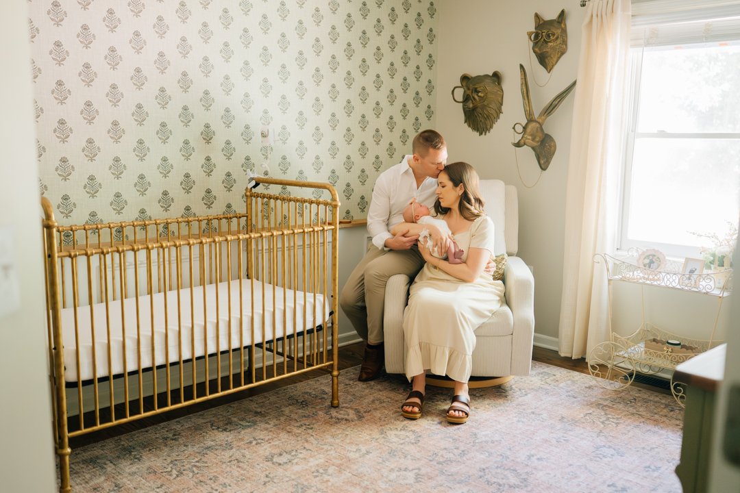    Travelers Rest in home newborn photographers capturing baby Charley with her parents in her nursery    Baby girl newborn photos with parents in a Travelers Rest SC nursery    Mom holding swaddled newborn baby girl beside an antique brass crib in T