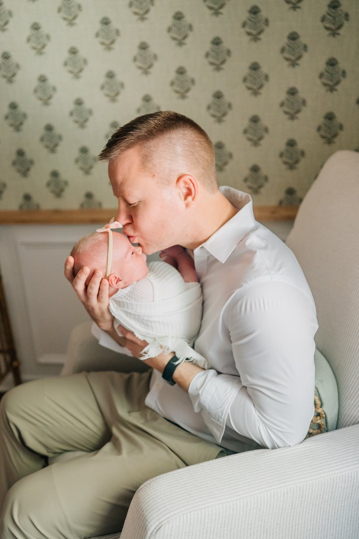    Travelers Rest in home newborn photographers capturing baby Charley with her parents in her nursery    Baby girl newborn photos with parents in a Travelers Rest SC nursery    Mom holding swaddled newborn baby girl beside an antique brass crib in T
