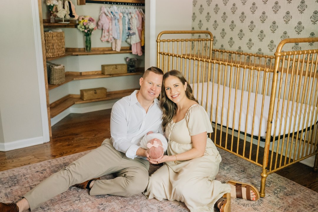    Travelers Rest in home newborn photographers capturing baby Charley with her parents in her nursery    Baby girl newborn photos with parents in a Travelers Rest SC nursery    Mom holding swaddled newborn baby girl beside an antique brass crib in T