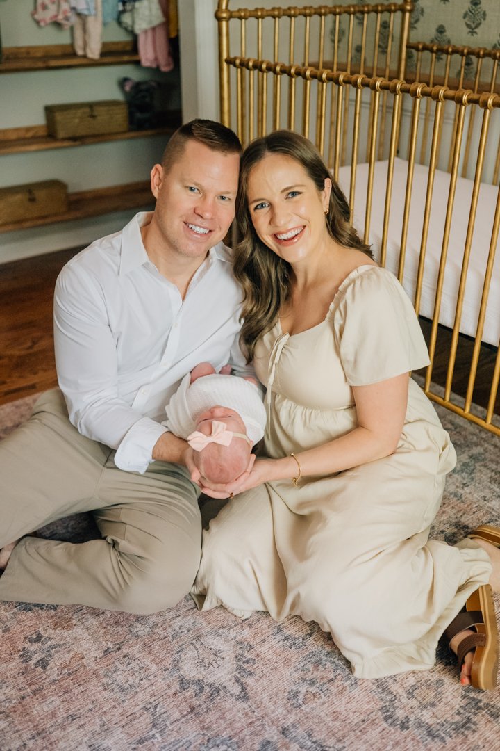    Travelers Rest in home newborn photographers capturing baby Charley with her parents in her nursery    Baby girl newborn photos with parents in a Travelers Rest SC nursery    Mom holding swaddled newborn baby girl beside an antique brass crib in T