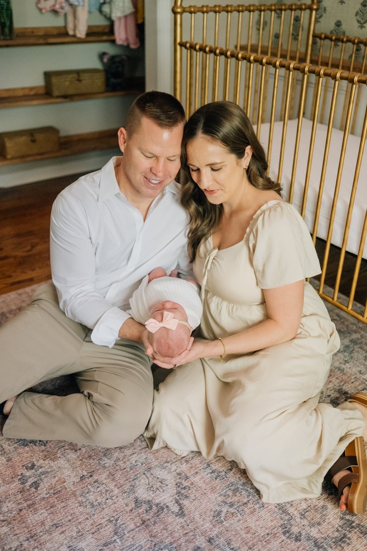    Travelers Rest in home newborn photographers capturing baby Charley with her parents in her nursery    Baby girl newborn photos with parents in a Travelers Rest SC nursery    Mom holding swaddled newborn baby girl beside an antique brass crib in T