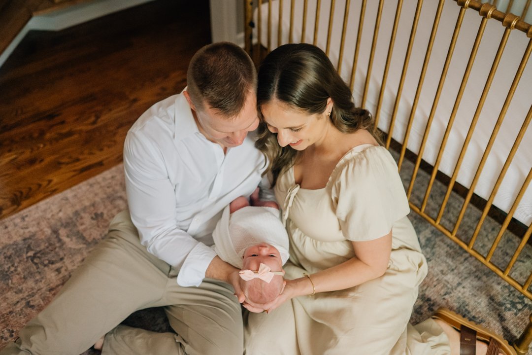   Travelers Rest in home newborn photographers capturing baby Charley with her parents in her nursery    Baby girl newborn photos with parents in a Travelers Rest SC nursery    Mom holding swaddled newborn baby girl beside an antique brass crib in T