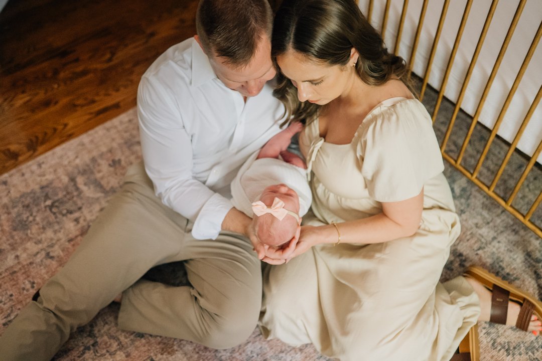    Travelers Rest in home newborn photographers capturing baby Charley with her parents in her nursery    Baby girl newborn photos with parents in a Travelers Rest SC nursery    Mom holding swaddled newborn baby girl beside an antique brass crib in T