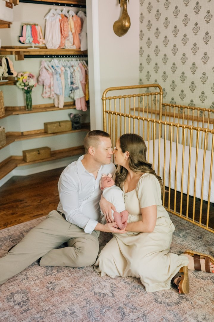    Travelers Rest in home newborn photographers capturing baby Charley with her parents in her nursery    Baby girl newborn photos with parents in a Travelers Rest SC nursery    Mom holding swaddled newborn baby girl beside an antique brass crib in T