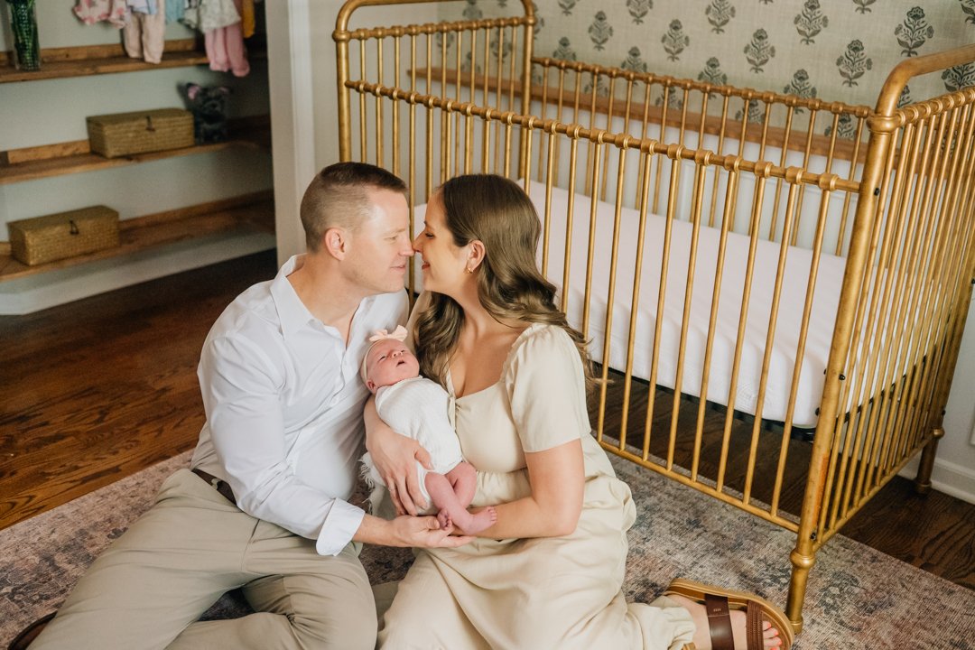    Travelers Rest in home newborn photographers capturing baby Charley with her parents in her nursery    Baby girl newborn photos with parents in a Travelers Rest SC nursery    Mom holding swaddled newborn baby girl beside an antique brass crib in T