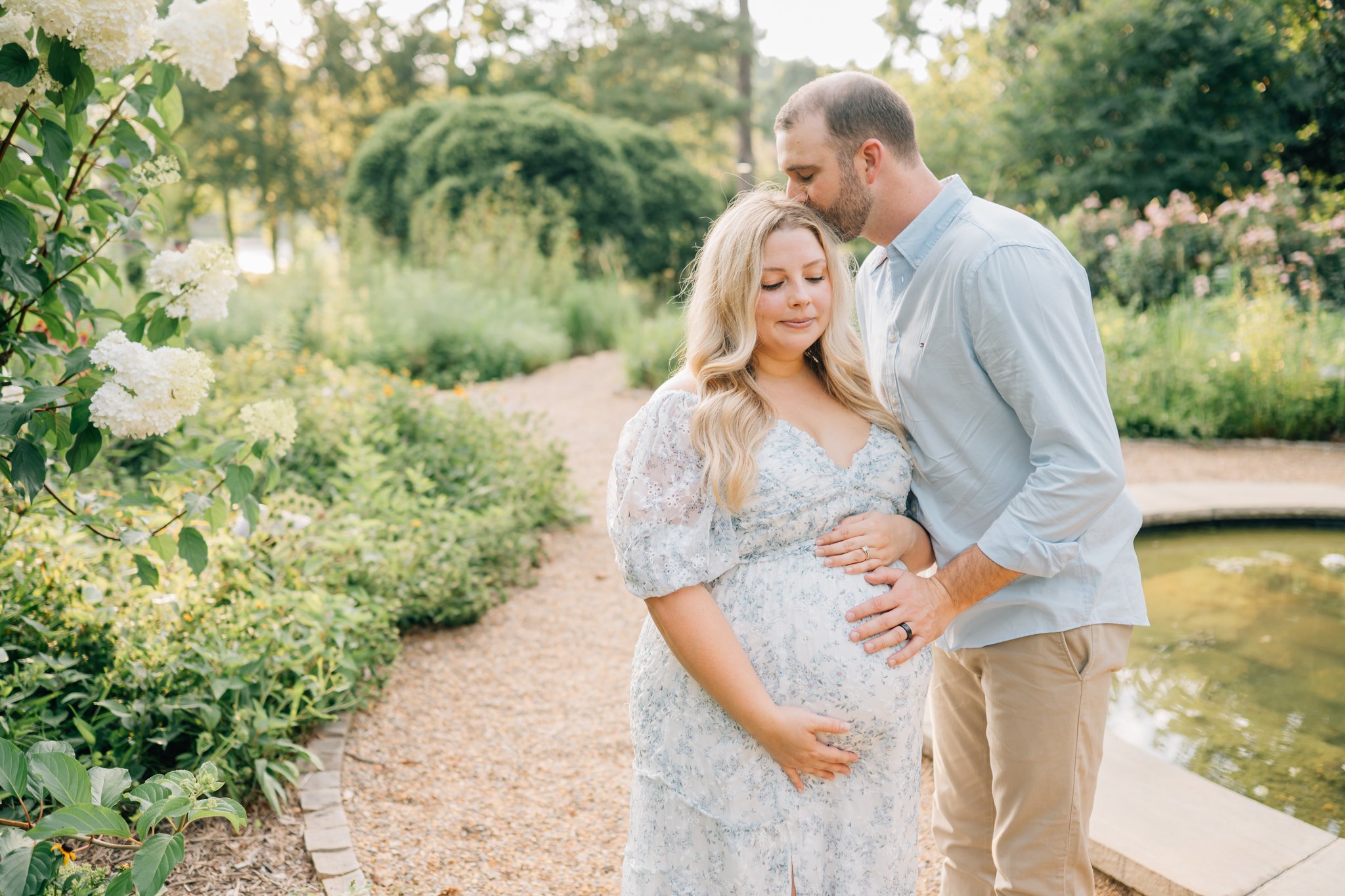 A man kissing a pregnant woman on the forehead in a garden