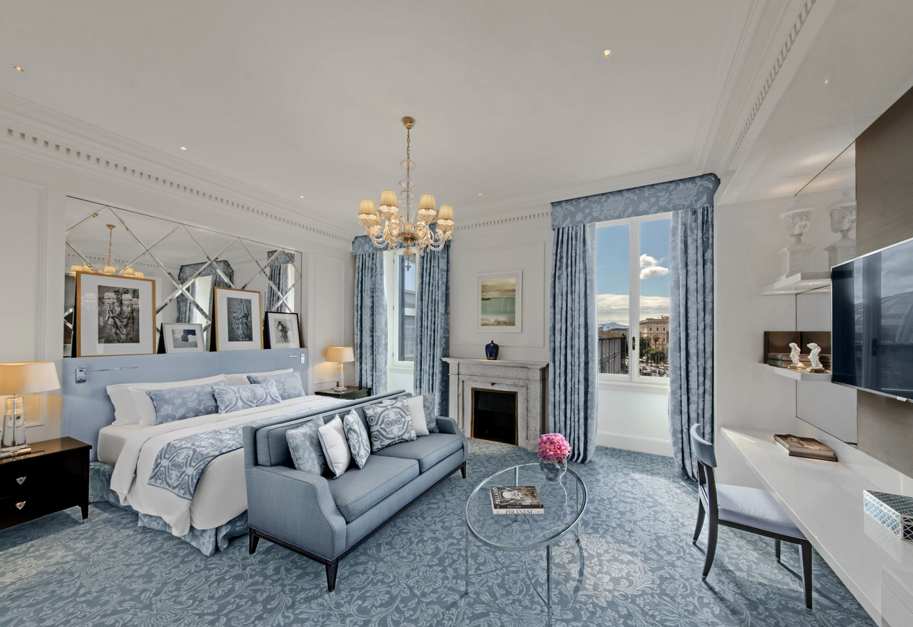 Blue and white room at St. Regis Rome, bed with sofa and pillows, coffee table, fireplace, chandelier