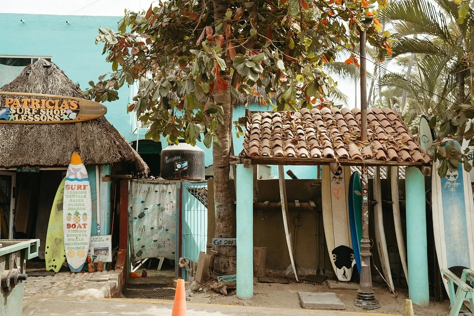 Colorful tropical surf shop photography featuring rows of surfboards, thatched and tiled rooftops, and palm trees in a laid-back beach town. Authentic surf culture and travel photography ideal for surf brands, outdoor lifestyle campaigns, beach desti