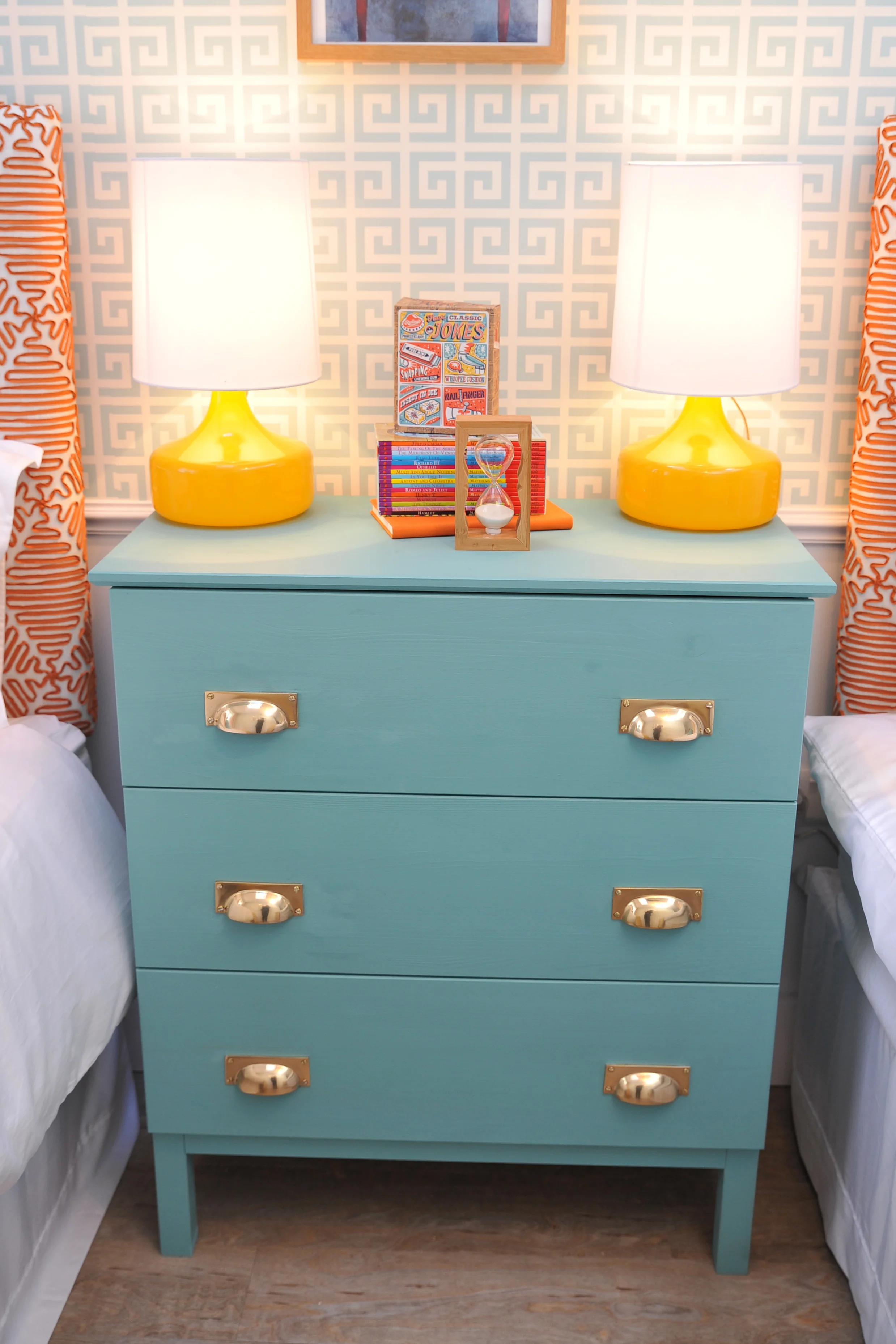 Upcycled turquoise chest of drawers with brass pull handles and two yellow table lamps.