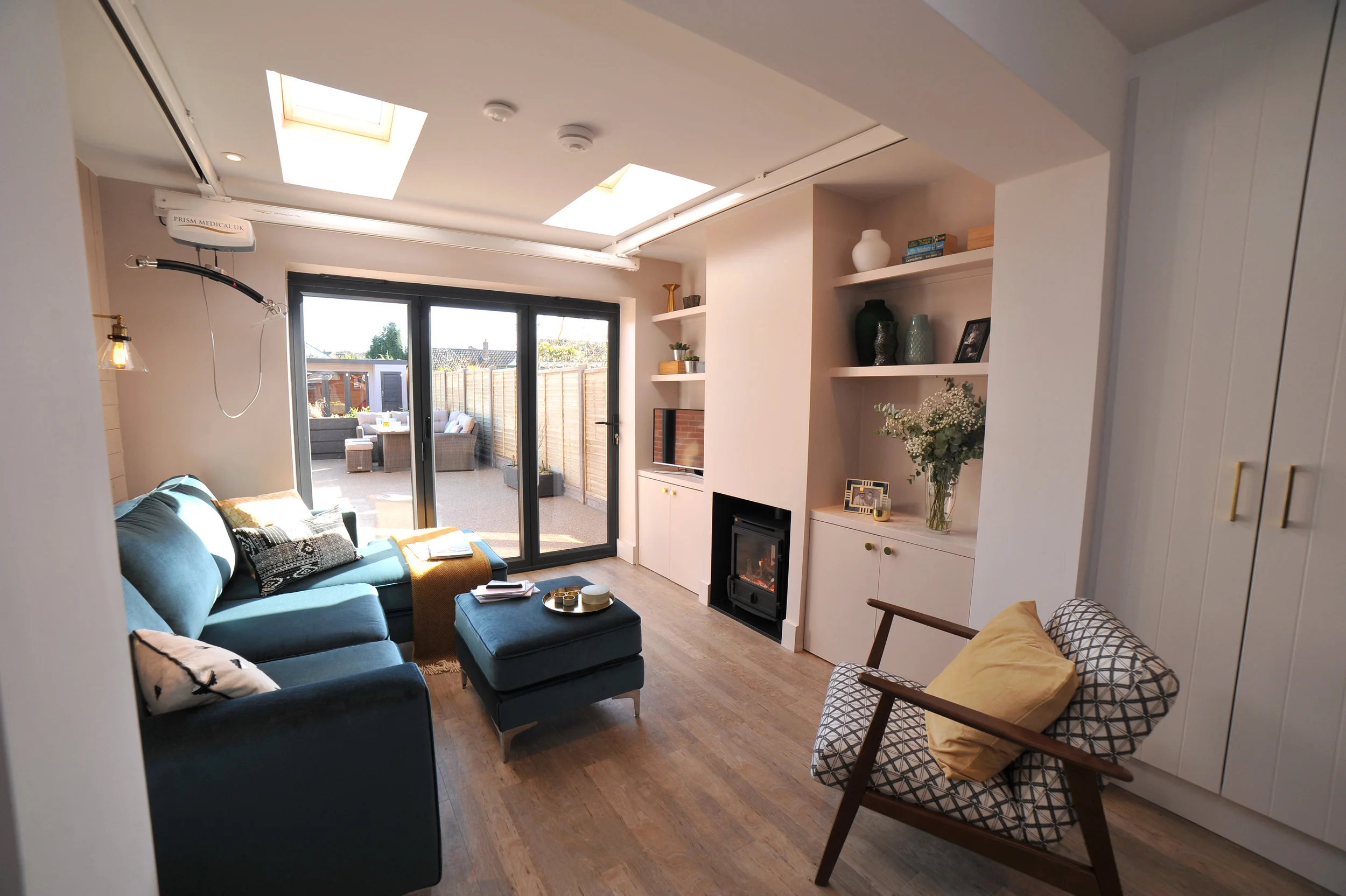 Blush pink living room with anthracite bifold doors, a teal corner sofa and geometric patterned armchair.