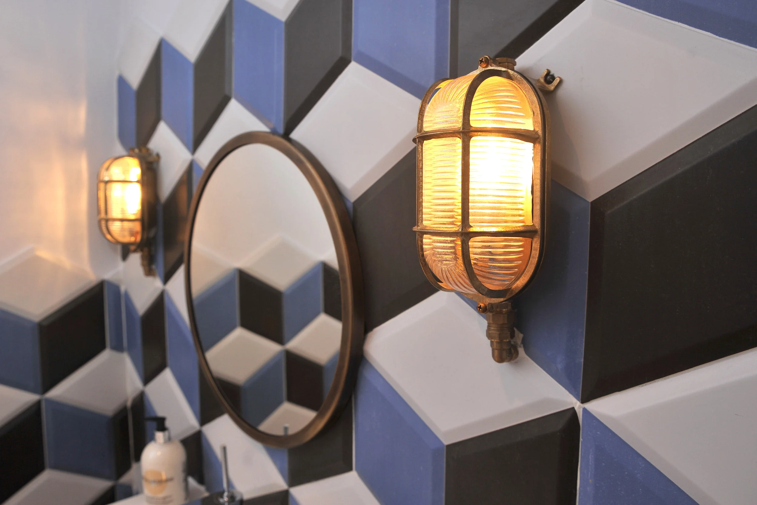 A bathroom with blue, black and white tiles with a brass mirror and wall lights on either side.