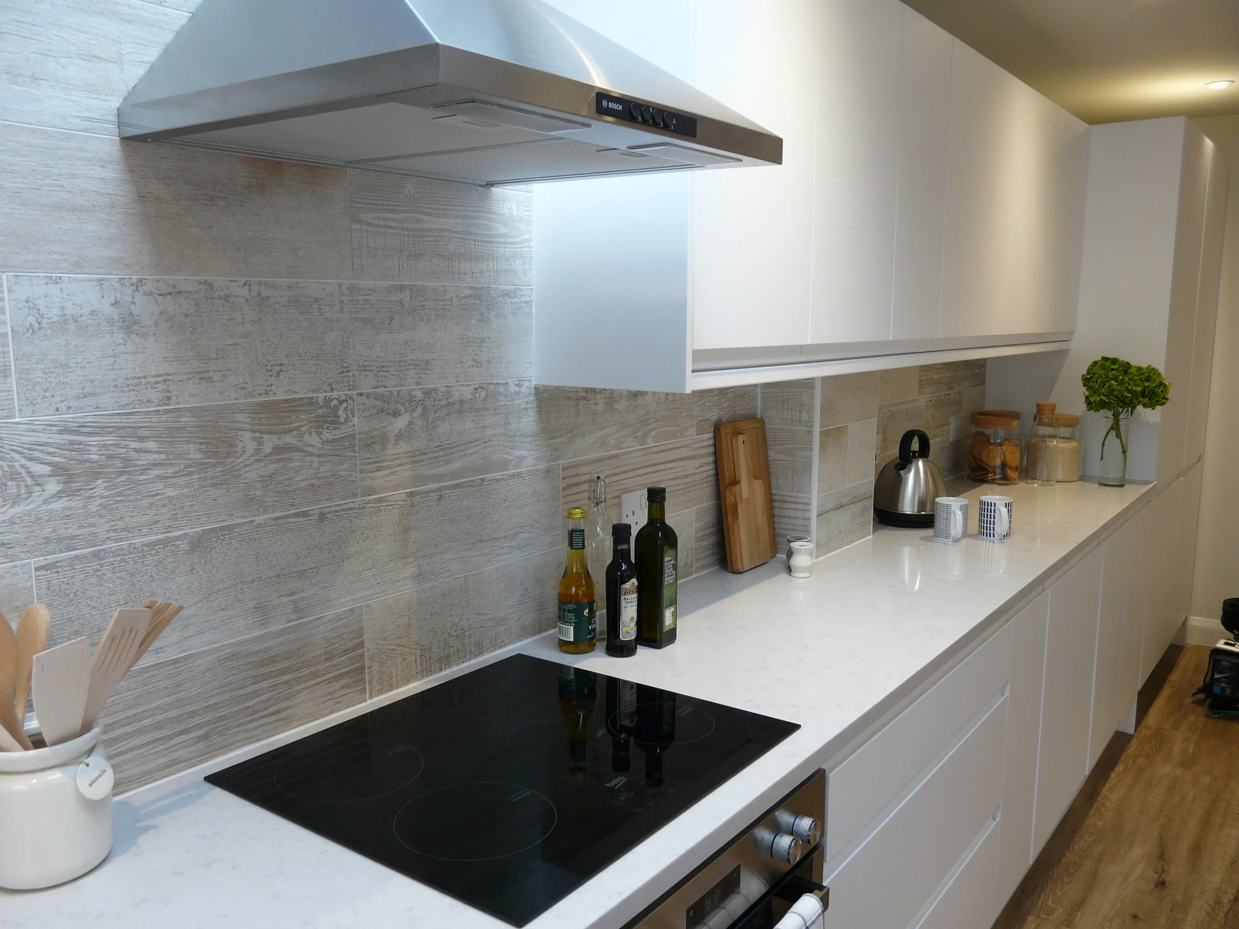 White gloss handleless kitchen with timber effect tile splash back
