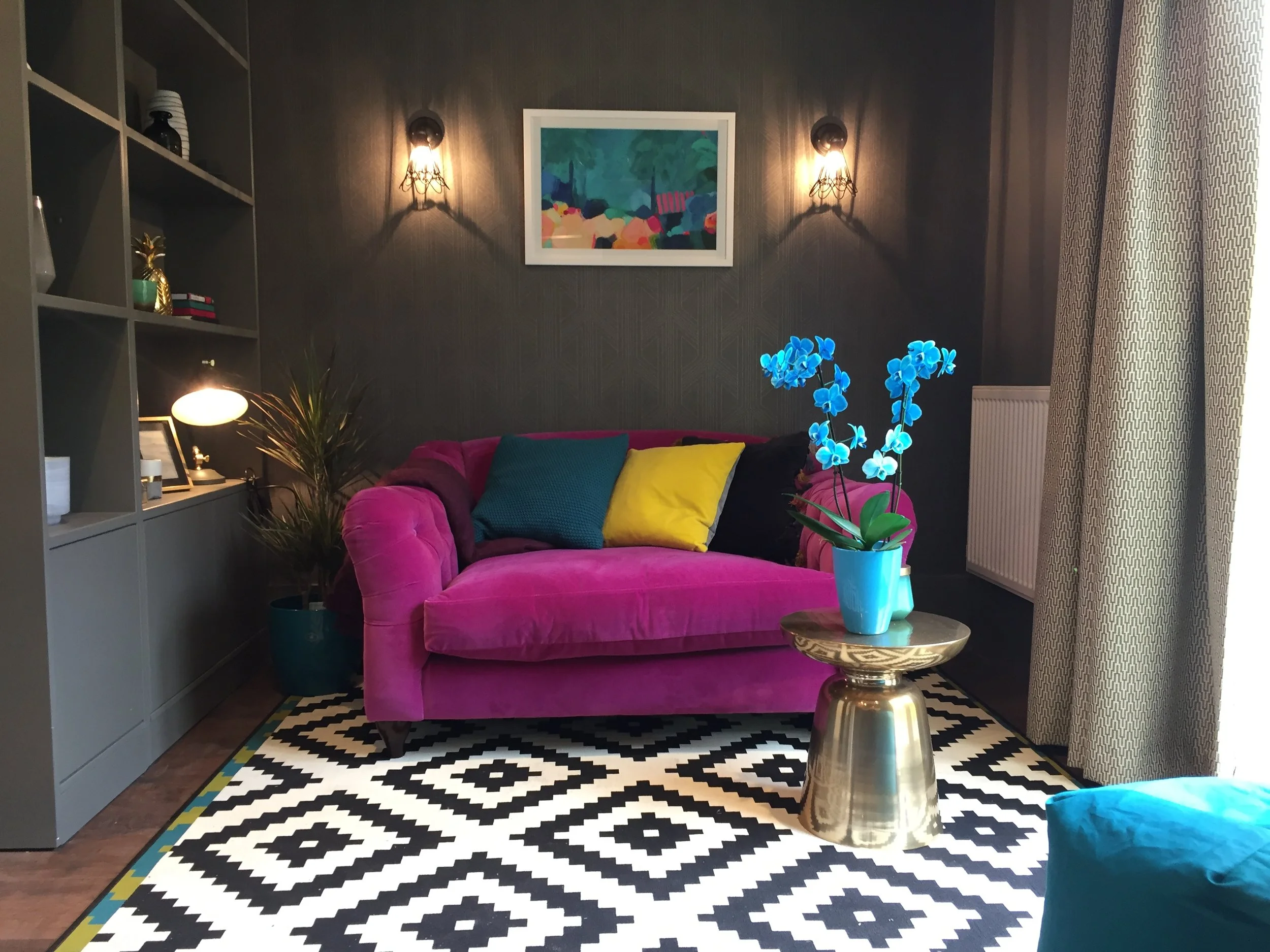 Grey living area with fuchsia coloured sofa and geometric rug.