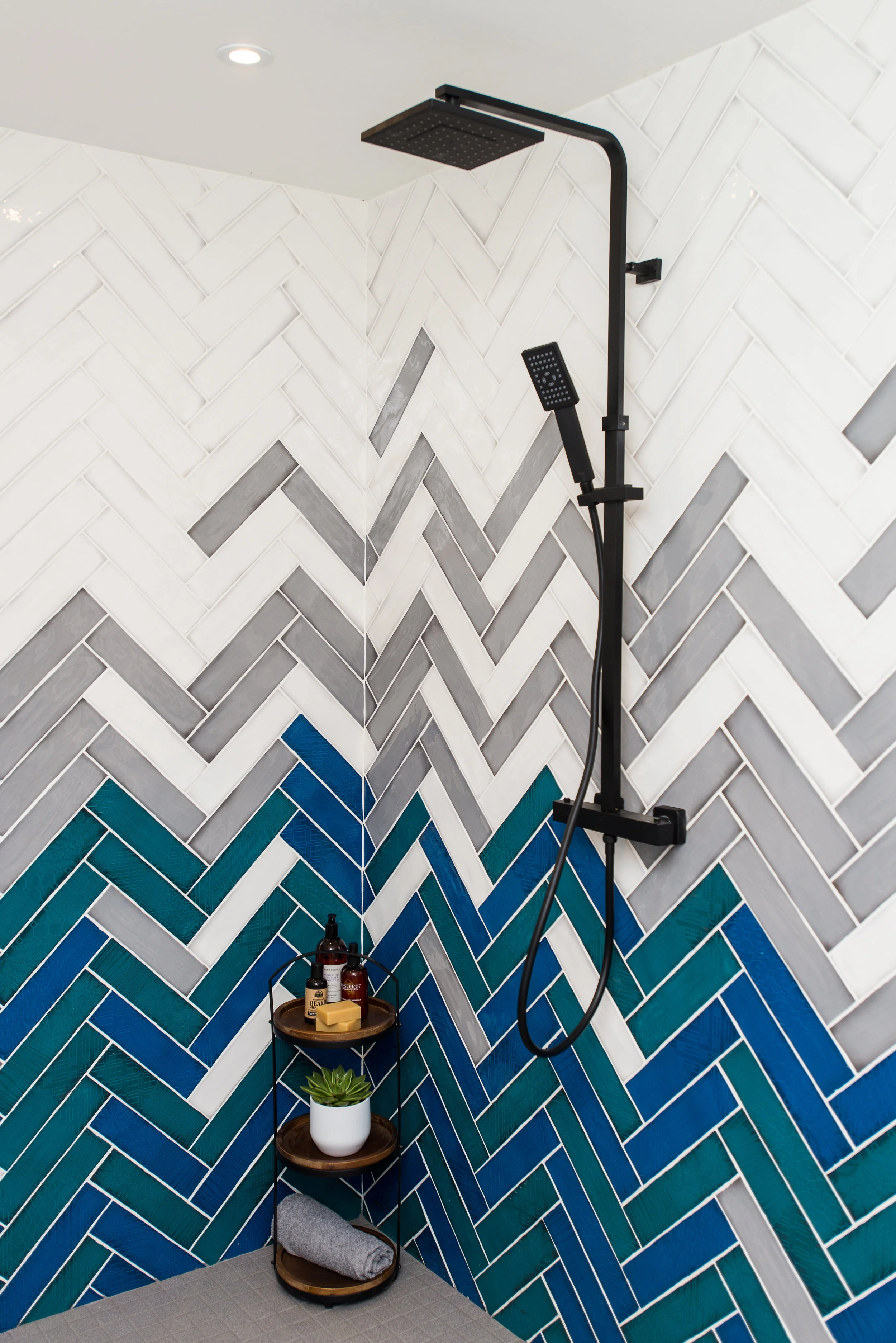 Herringbone tiled bathroom in blue, green, grey and white with black shower fitting