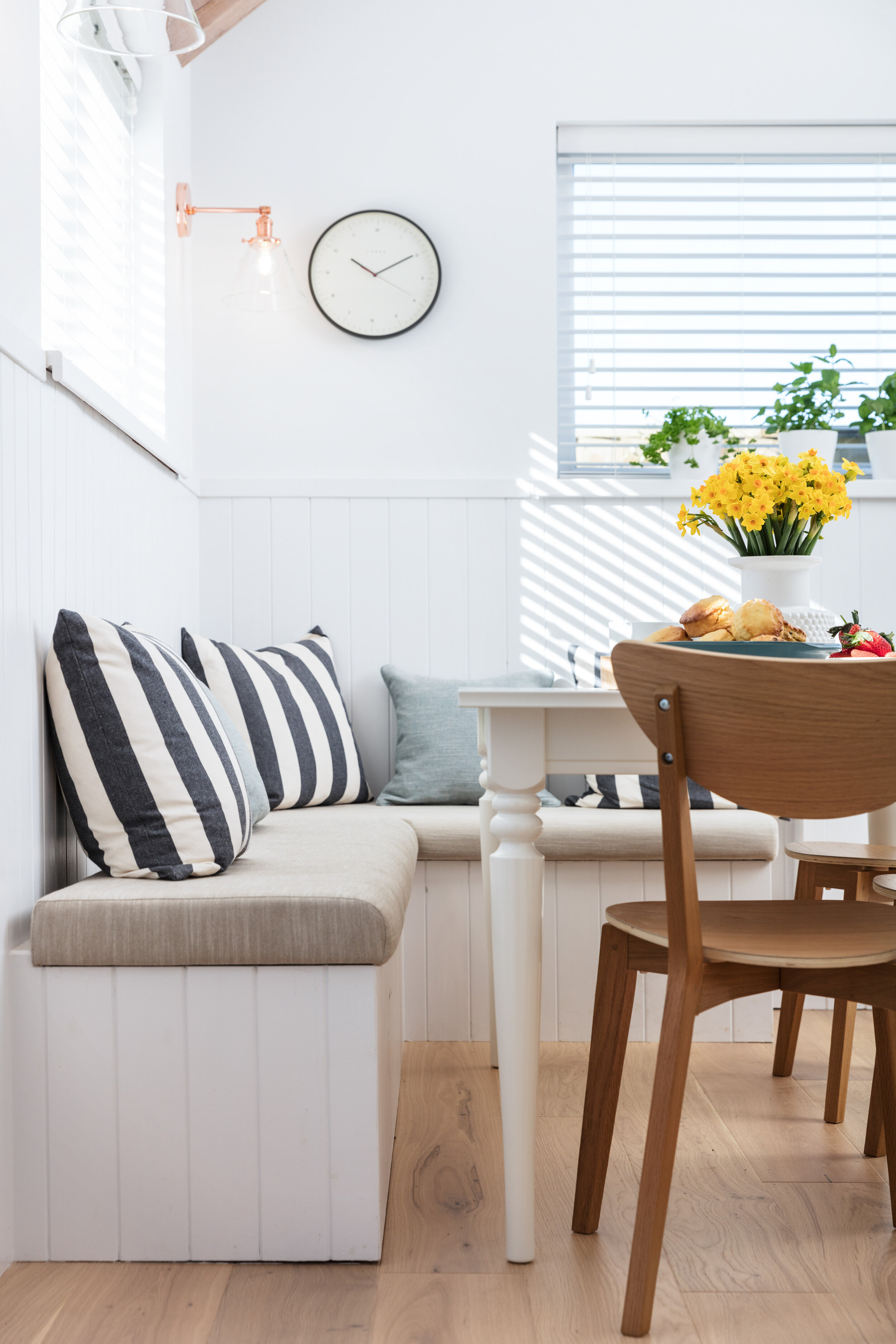 Bright white dining room with tongue and groove panelling on the upholstered banquette and walls.