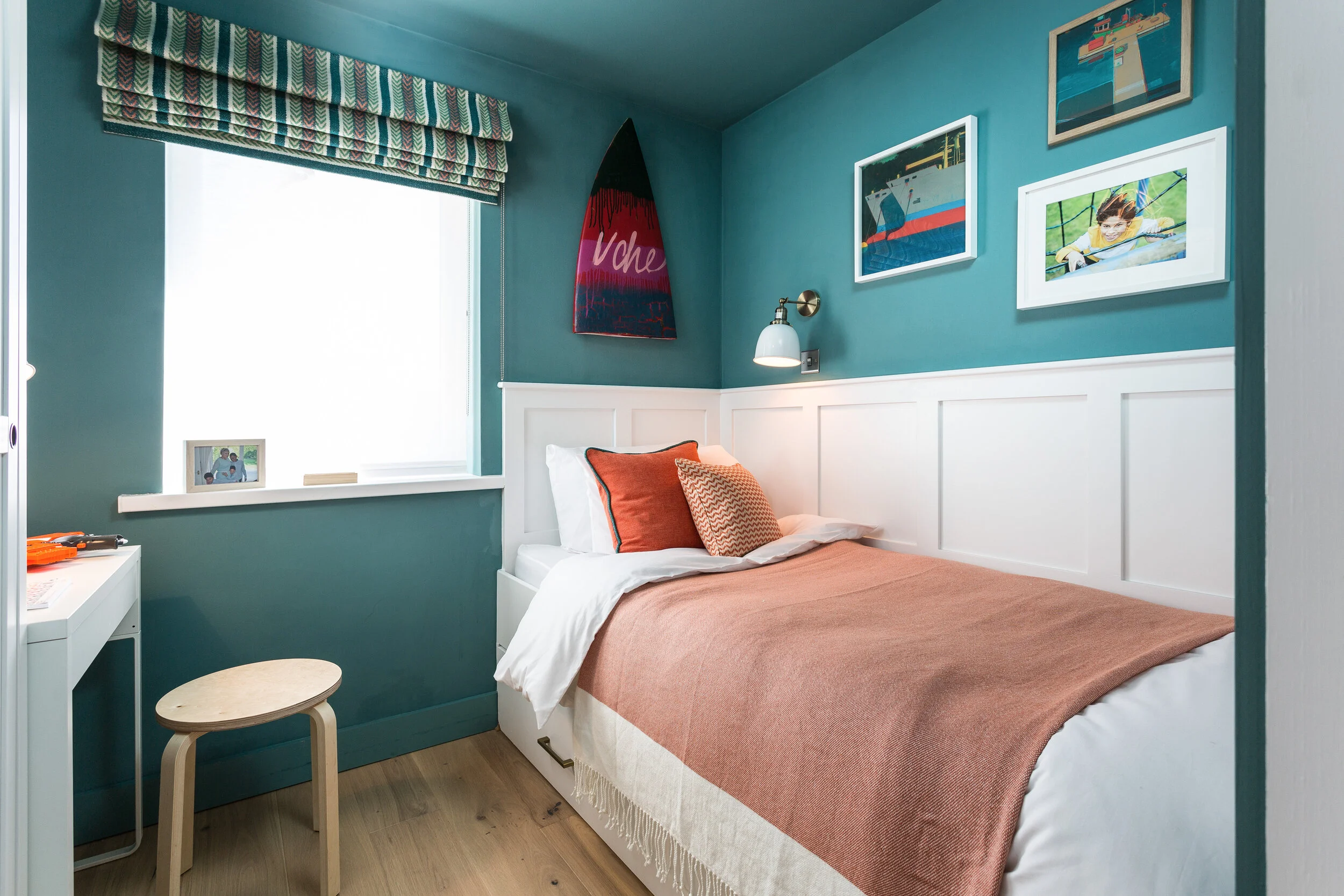 Turquoise bedroom with a white built in bed with orange soft furnishings