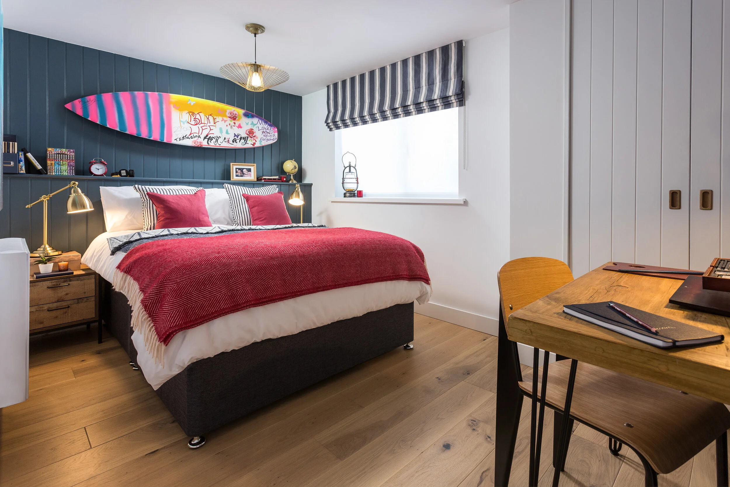 Double bedroom with a charcoal painted tongue and groove feature wall with a surfboard above the bed