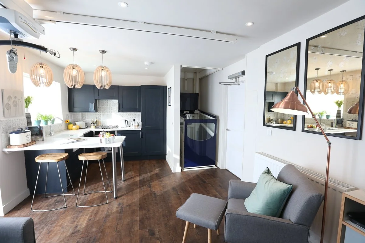 White accessible kitchen with navy shaker kitchen units, a blue through floor lift and ceiling track hoist