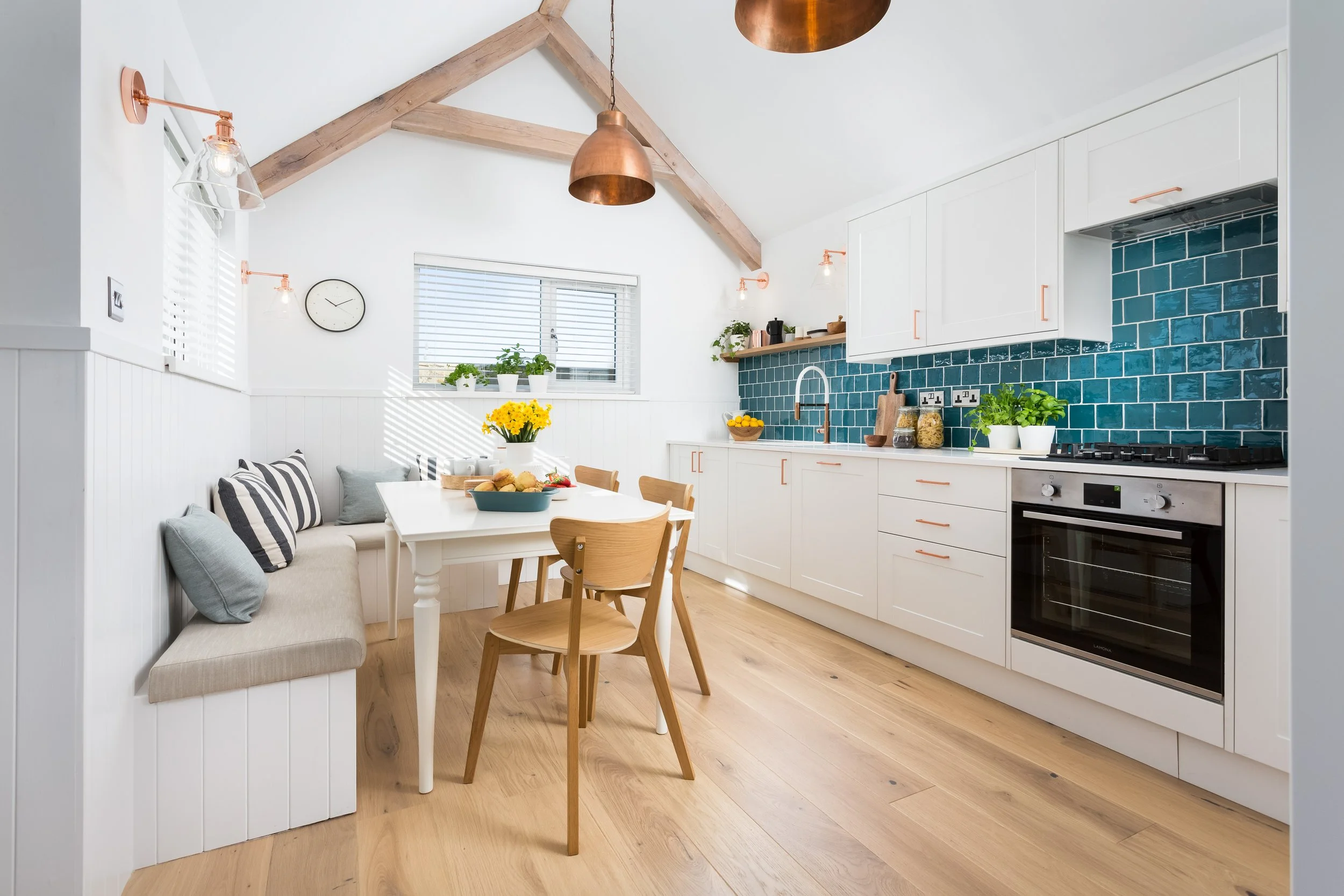 White kitchen diner with square turquoise splash back tiles and an upholstered built in banquette seat