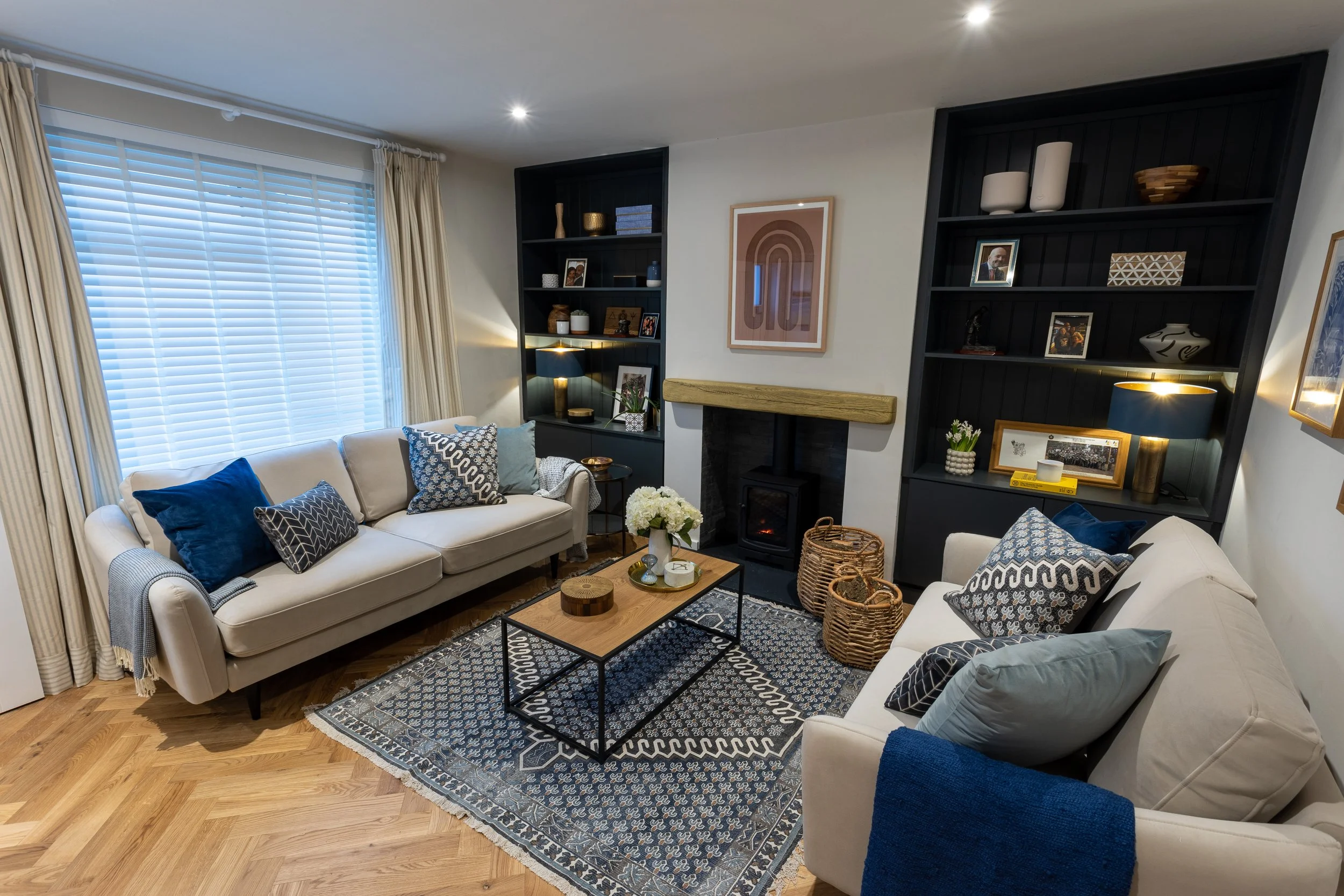 Living room with black built in shelving on each side of the chimney breast. Two beige sofas with blue cushions and a matching blue rug between them